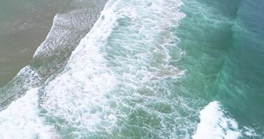 drone aerial view of the ocean swell on the shore of a beach with foam in the waves, aerial footage over a beach day of surf and foam. Sea background video