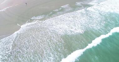 drone aerial view of the ocean swell on the shore of a beach with foam in the waves aerial footage flying over a beach day of surf and foam. Sea background video