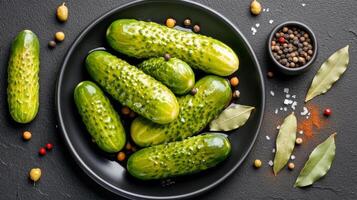 Whole pickled cucumbers glisten with brine, surrounded by spices on a dark plate, creating a trendy snack photo