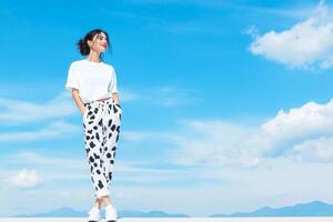 A young woman stands outside in cow print pants and sneakers, enjoying the sunshine and beautiful sky with clouds photo