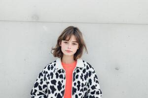 A girl stands confidently in a cow print jacket, showcasing her unique style against a cool concrete backdrop photo