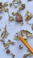 Close-up of sharpened yellow pencil with wood shavings on white background, drawing heart shape. Creative education or art concept captured in macro shot video