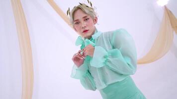 A model in a mint green outfit with sheer sleeves and a bow tie, posing elegantly against a soft, neutral backdrop. video