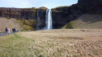Tourists walking to and from the famous Seljalandsfoss waterfall in Iceland video