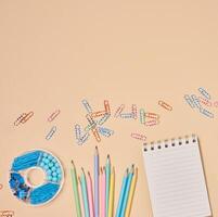 Flat lay of colorful school and office supplies including pencils, paper clips, notebooks on a peach background. Creative workspace concept. photo