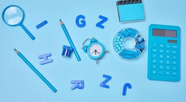 Blue stationery, learning items letters, magnifying glass, supplies, and an alarm clock on a blue background. Education, time, and study concept photo
