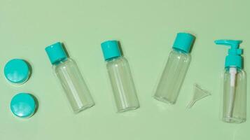 Top view of set of five transparent cosmetic bottles and two round jars with turquoise lids and one funnel, light green background photo