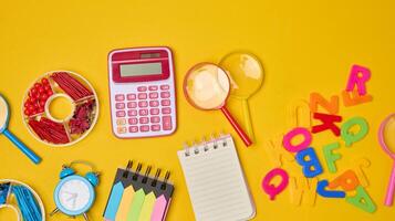 Collection of colorful school supplies, building bricks, letters, and learning items scattered on a yellow background. Play photo
