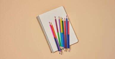 Top view of an open notebook with pastel-colored pencils on a beige background. photo