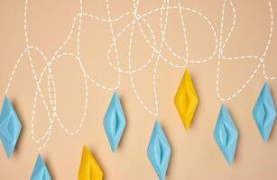 A creative composition featuring blue and yellow paper boats with dashed lines trailing behind them on a beige background, journey or exploration photo