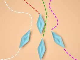 Top view of four blue paper boats following different dotted lines on a beige background. photo