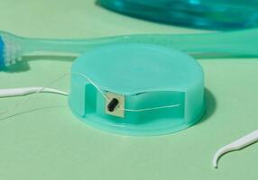 A turquoise dental floss container with floss extended, along with white floss picks, are shown on a light green background photo