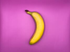 One bright yellow banana, lying vertically on a purple background, top view, center of image turned left photo