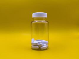 White pills in a transparent jar on a yellow background, front view, against virus and colds photo