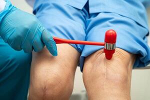 doctor knock on knee reflex nerve for check and treatment senior patient photo