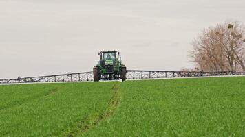 Modern tractor spraying green wheat field, wide boom arms and fresh vegetation, Precision agriculture in action, boosting early crop development with accuracy video