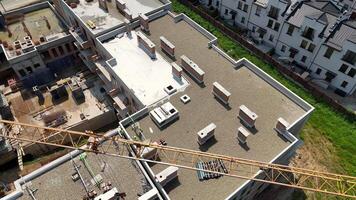 Aerial view of residential complex construction with crane over rooftops, Workers and materials visible on upper levels of multistory concrete structure video
