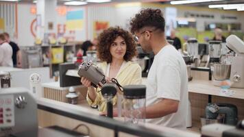 Young couple browsing kitchen appliances inside modern electronics store, comparing coffee maker features with collaborative teamwork while moving in slow motion video