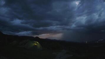 Dramatic timelapse of couple camping in tent atop mountain as thunderstorm brews, with glowing shelter against dark clouds and lightning in distant horizon.Concept hikers under lightning sky isolated. video