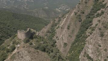 Ancient stone fortress ruin on mountain ridge surrounded by forested valleys and distant peaks in summer daylight, aerial view. video