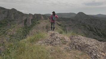 Woman standing alone on rocky mountain edge, gazing at vast landscape of ridges and valleys, symbolizing freedom, achievement, and self-reflection in powerful natural setting video