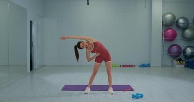 niña atleta se involucra en dinámica extensión ejercicios en un moderno gimnasio ambiente durante un aptitud rutina video