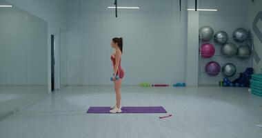Girl athlete performs reverse lunges with dumbbells in a bright gym setting during a training session video