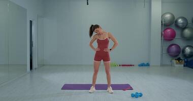 Girl athlete performs head rotations in fitness studio during workout session while focusing on neck flexibility and strength video