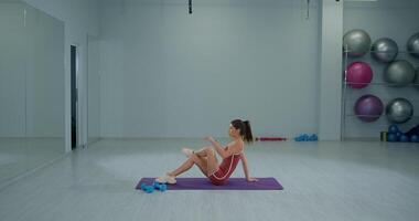 Girl athlete performs seated piriformis stretch in a modern gym during a workout session for flexibility and recovery video
