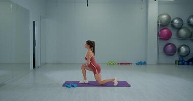 Girl athlete performing a kneeling quad stretch in a gym environment during a training session for flexibility and strength video