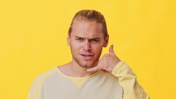 A stylish young man with mixed ethnicity gestures a phone call sign with his hand. He stands against a bright yellow backdrop, exuding a relaxed and friendly vibe typical of Gen Z. video