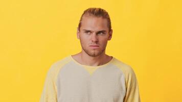 A guy with African and Caucasian features displays a serious expression in front of a bright yellow backdrop. He is wearing a casual, light-colored sweater, conveying an intense mood. video