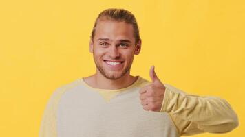 A young man with an enthusiastic smile and a confident thumbs up is set against a vibrant yellow background. His casual attire complements the cheerful atmosphere, capturing positivity. video
