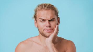 A young man with a mixed heritage shows a surprised expression while touching his face, suffering from toothache The background is a solid light blue, highlighting his features and emotions. video
