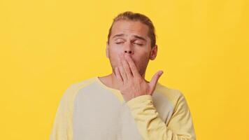 A man with mixed heritage expresses a lighthearted moment, playfully yawning. He stands against a vibrant yellow backdrop, capturing a sense of casual charm and youthful energy. video