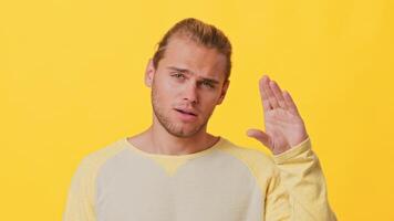 A young man of mixed descent shows excitement with a raised hand, set against a vibrant yellow backdrop. His expression captures enthusiasm and joy in a casual setting. video