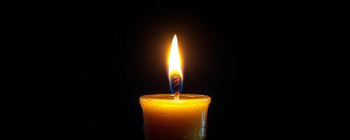 Candle flickering in dark background. A single candle burns brightly in a dark setting, creating a warm and serene atmosphere with its gentle glow. photo