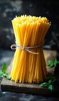Bundle of dry spaghetti. A bundle of dry spaghetti rests on a rustic wooden surface, tied with twine, surrounded by fresh green basil leaves. photo