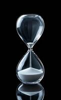Elegant glass hourglass captures time. A clear glass hourglass stands on a smooth surface, filled with fine white sand, measuring time in an artistic way. photo