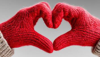 Hands in red gloves create a heart shape. Two hands wearing knitted red gloves form a heart shape against a neutral background, symbolizing warmth and affection. photo