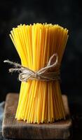 Dried spaghetti bundled on wooden board. A bundle of uncooked spaghetti tied with twine rests on a rustic wooden surface, showcasing its vibrant yellow color. photo