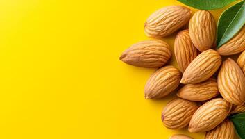 Almonds on yellow surface. Fresh almonds arranged on a vibrant yellow background with green leaves adding a natural touch. photo