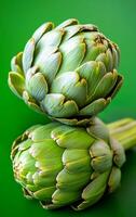 Artichokes stacked on a green surface. Two fresh artichokes are stacked, showcasing their vibrant green color against a smooth green background. photo