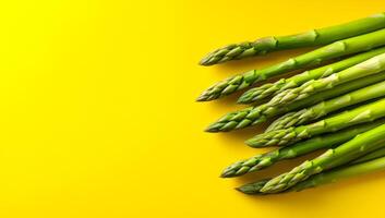 Asparagus on yellow backdrop. Fresh green asparagus spears arranged on a vibrant yellow surface, highlighting their texture and color. photo