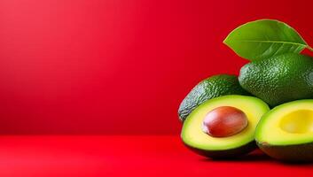 Avocados on a bright backdrop. Ripe green avocados with one halved, showcasing smooth flesh and seed against a bold red backdrop. photo