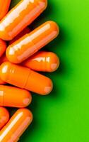 Bright orange capsules on green surface. A collection of bright orange capsules is arranged on a vibrant green surface, showcasing their smooth texture. photo