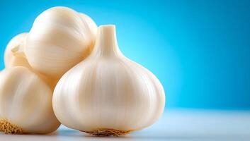 Fresh garlic bulbs arranged on a table. Clusters of white garlic bulbs are displayed against a light blue backdrop, showcasing their smooth skin and texture. photo