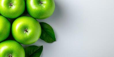 Fresh green apples on a light surface. Crisp green apples with leaves arranged on a smooth surface, showcasing their vibrant color and freshness. photo