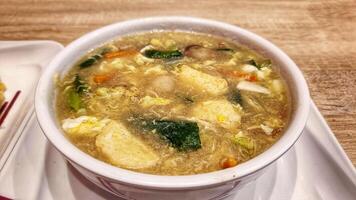 soup with thick broth and pieces of meatballs, seafood, and green vegetables served in white bowl photo