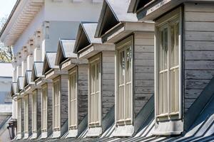 Dormer windows in a row on the pitched roof of a historic building, illuminated by the sun. photo